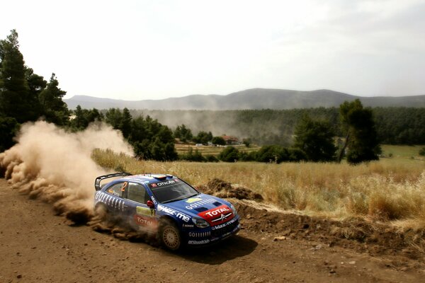 Un automóvil Citroën que participa en un Rally conduce por un camino de tierra levantando una columna de polvo