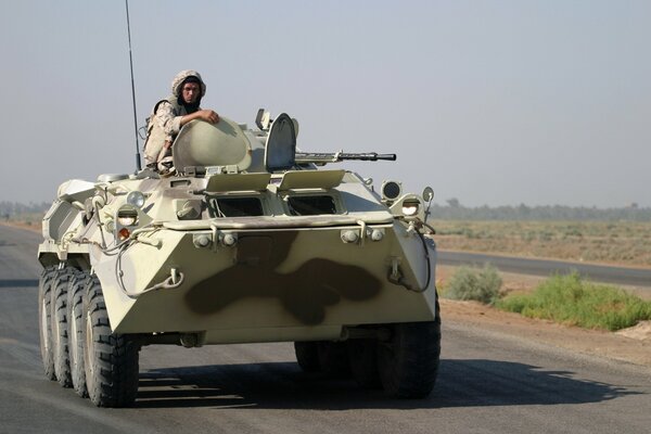 A soldier in camouflage riding in a tank on the road