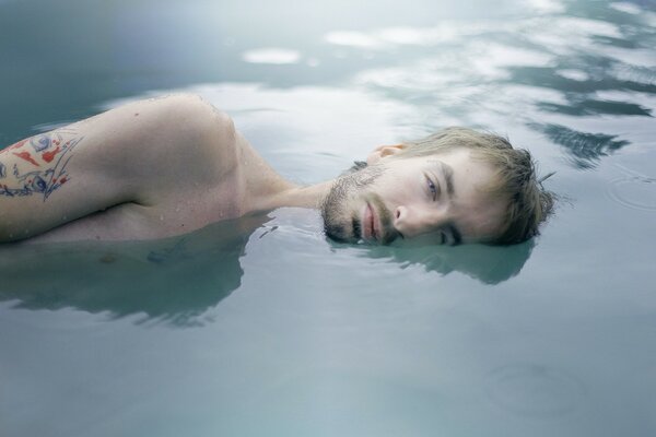 Im Wasser liegender Mann mit Tattoo