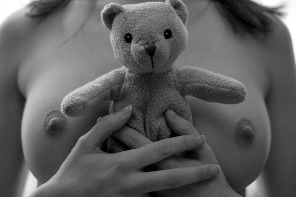 A girl with bare breasts hugs a teddy bear to her