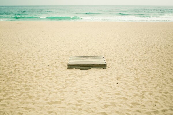 A box on the yellow sand of the beach. Turquoise waves