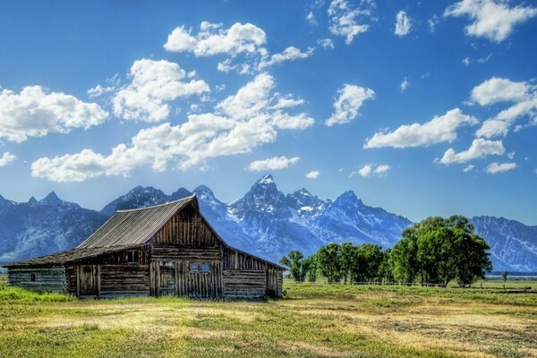 Maison en bois dans un champ sur fond de montagnes