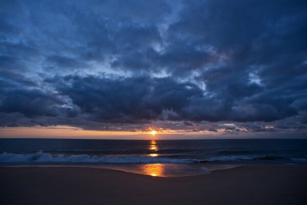 Piaszczysta plaża i delikatne morskie fale w romantycznym niebieskim zachodzie słońca