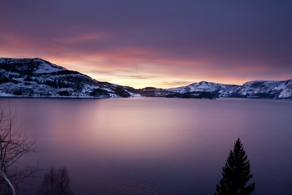 Lago lila en el fondo de las montañas cubiertas de nieve a la luz del atardecer