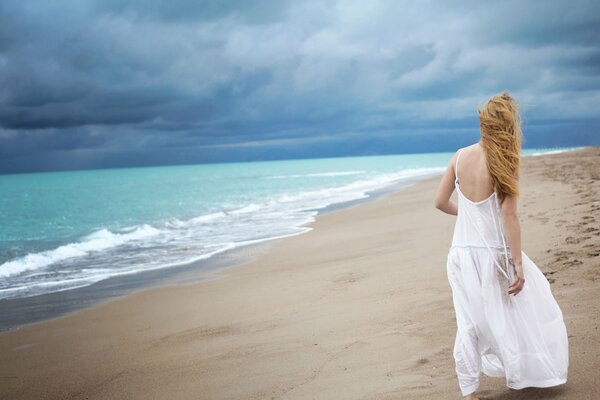 Lonely girl in a white dress by the sea