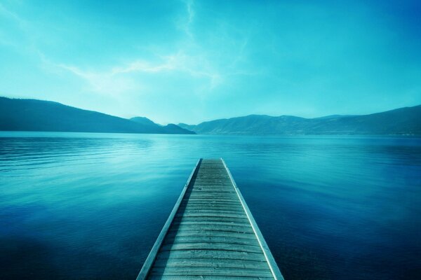 A bridge in the lake opposite the mountains in blue tones