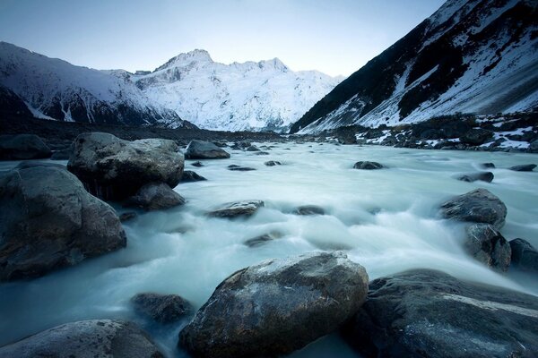 Río que fluye en el fondo de las montañas cubiertas de nieve