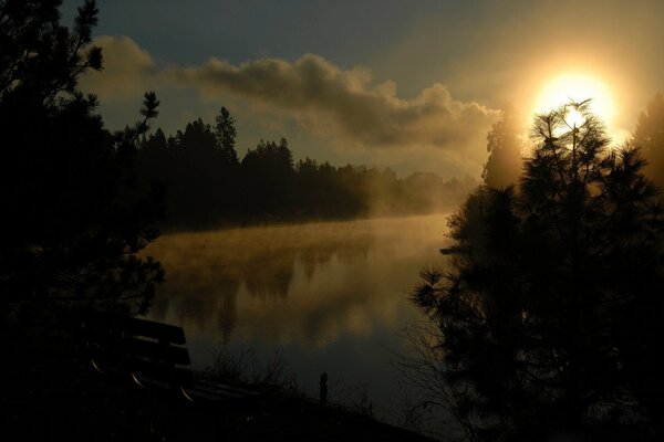 Eine Bank am Fluss und ein schöner Himmel mit Sonne