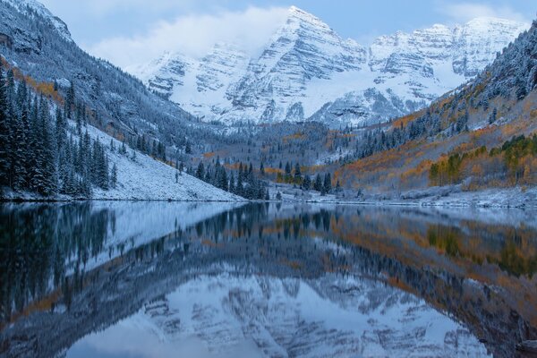 Lago de montaña con árboles de otoño y nieve