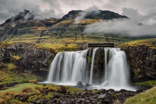 Wasserfall auf einem Berg mit grauen Wolken in Island