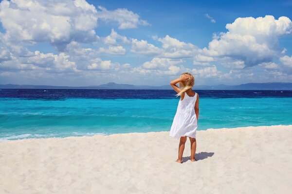 Imagen de una chica con un vestido blanco en la playa cerca del mar azul
