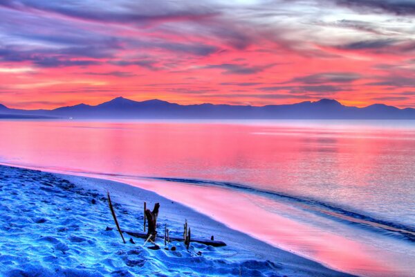 The seashore against the background of a scarlet sunset and mountains