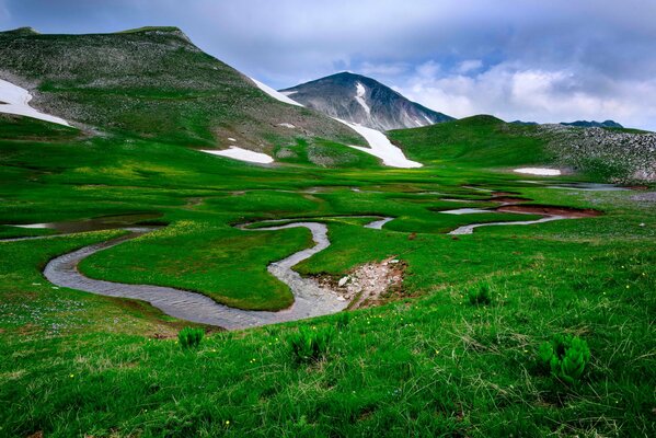 Bergpanorama mit einem gewundenen Fluss und grünem Gras