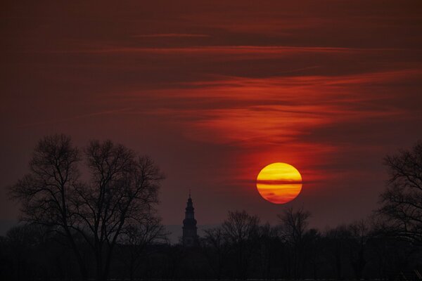 A bloody sky and a huge yellow moon, black silhouettes of turrets and trees