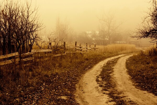 Ländliche Straße entlang eines alten Holzzauns, in Nebel versunkene Umrisse von Häusern und Bäumen