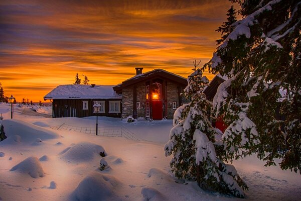 A cool sunset is depicted in Nice. The landscape includes a house, a snow sky, which are dressed up in winter colors. nature burns delightfully turning white snow into an extension of the orange sky