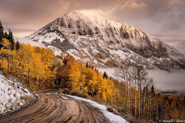 The road to the mountains against the background of the autumn forest