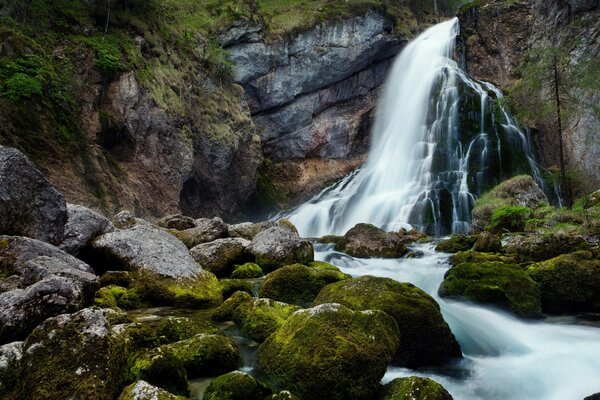 Waterfall descending from the mountains, stones overgrown with moss