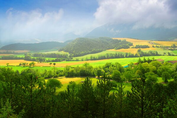 Green fields, houses and trees against the background of mountains, reaching peaks into the sky