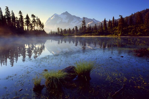 Mountains, fog, fir trees are visible on the lake