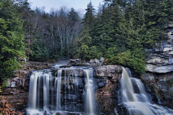 Wasserfall von einer Klippe auf dem Hintergrund eines dunklen Waldes