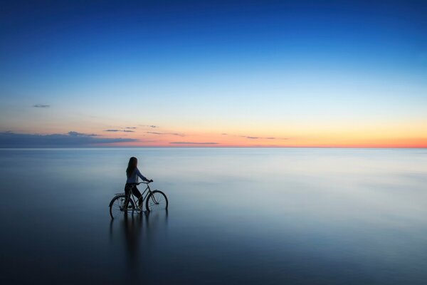 A girl with a bicycle enters the water