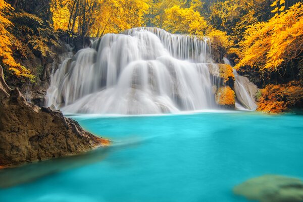 Herbstliche Wasserfalllandschaft am blauen See, umgeben von gelbem Wald