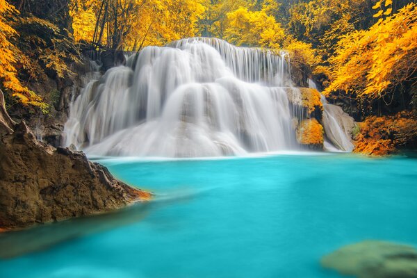 Paesaggio autunnale di una cascata su un lago blu circondato da una foresta gialla