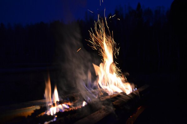 Sparks fly off from the flame of the fire by the campfire