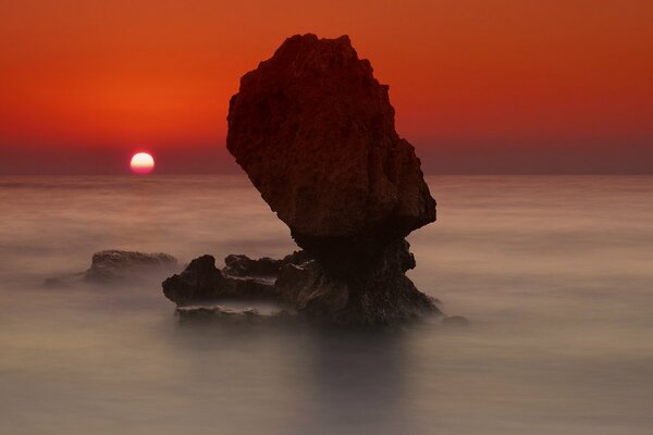 Sonnenuntergang auf einem Felsen im Meer Hintergrund