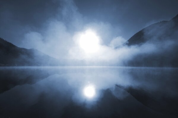 En la niebla, el sol se refleja en el lago