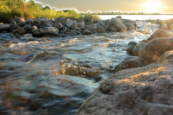 Ein schneller Wasserfluss durch die Steine zur Sonne. Foto des Flusses