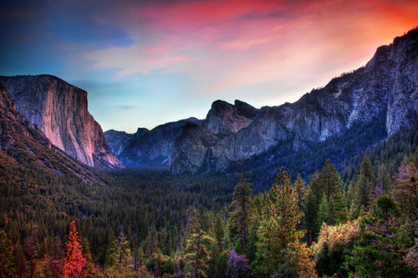 Un valle de belleza mágica con increíbles tonos de rocas y un bosque multicolor en primer plano con un cielo azul y rojo