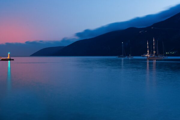 Sonnenuntergang aus der Bucht. Grünes Licht des Leuchtturms in der Ferne