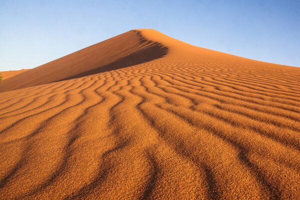 A desert with a pattern on the sand in the form of wavy lines against a blue sky background