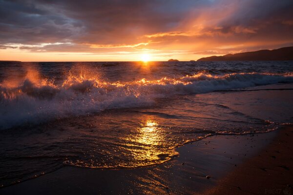 Schöner Sonnenuntergang vor dem Hintergrund der Wellen, die am sandigen Ufer vorbeifliegen