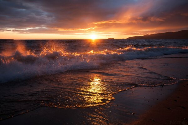 A beautiful sunset against the background of waves rushing onto the sandy shore