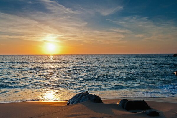 Stones in the embrace of beach sand under the rays of sunset