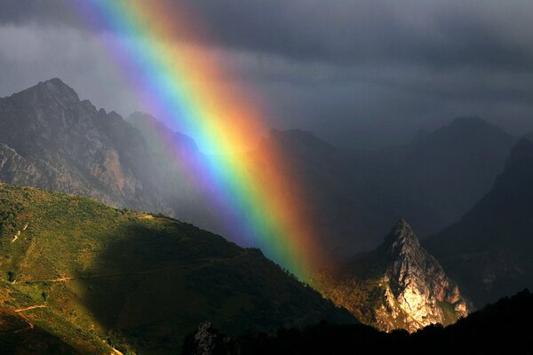 Ein Regenbogen von bewölktem Himmel an den Hängen der Berge