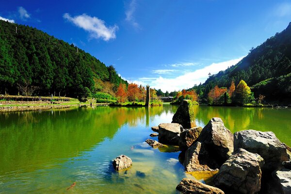 Beautiful view of the water with rocks protruding from it, blue sky and red trees in the distance