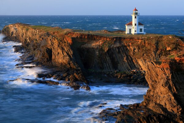 Bella vista del faro che si infrangono sulle onde della costa rocciosa