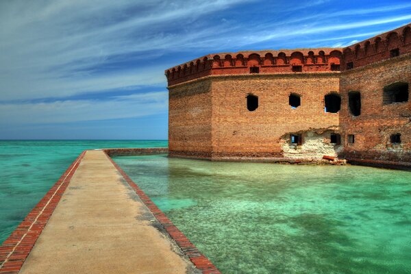 A bridge leading to the ruins of the fort through clear waters