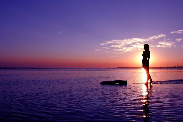 Foto de una niña en el mar en el fondo de la puesta de sol