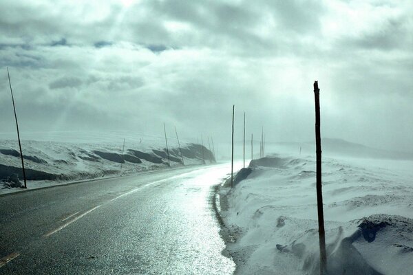 La luz se abre paso a través de las nubes. Carretera de invierno con nieve en las carreteras