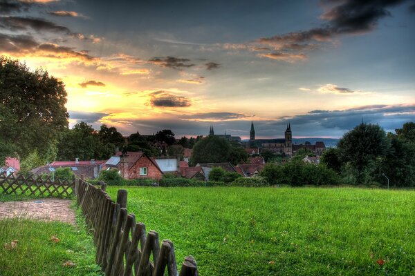 Derrière le champ vert, un petit village sous le ciel pendant le coucher du soleil