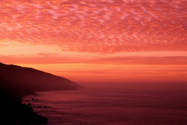 Purpurroter Sonnenuntergang am Meer mit niedrigen Wolken