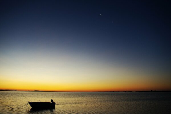 A lonely boat in the sea, against the background of the sunset sky