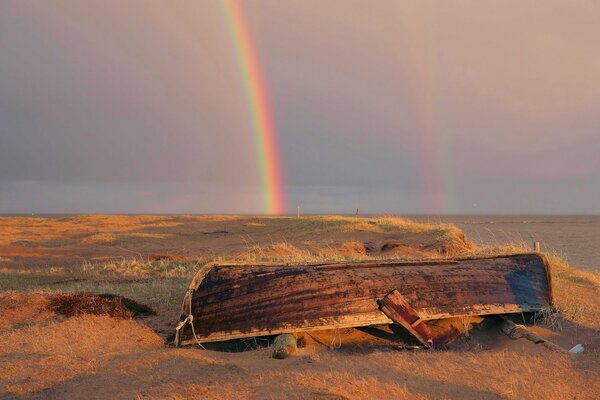 Bateau inversé sur une plage de sable sur fond d arc-en-ciel