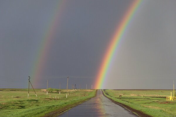 Double arc-en-ciel. Route au milieu des prairies