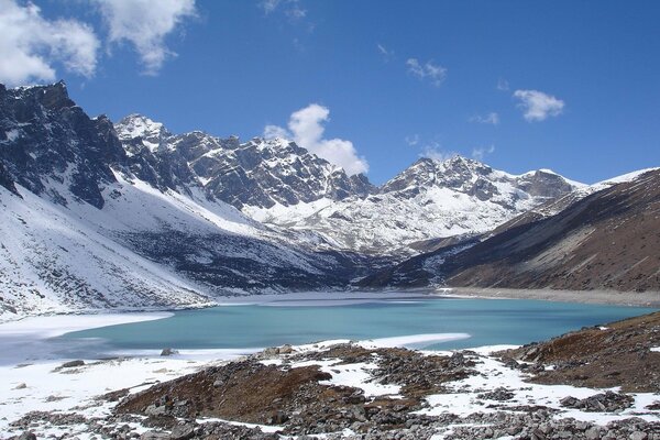 Ein Bergsee mit einer Eiskante inmitten schneebedeckten Berggipfeln